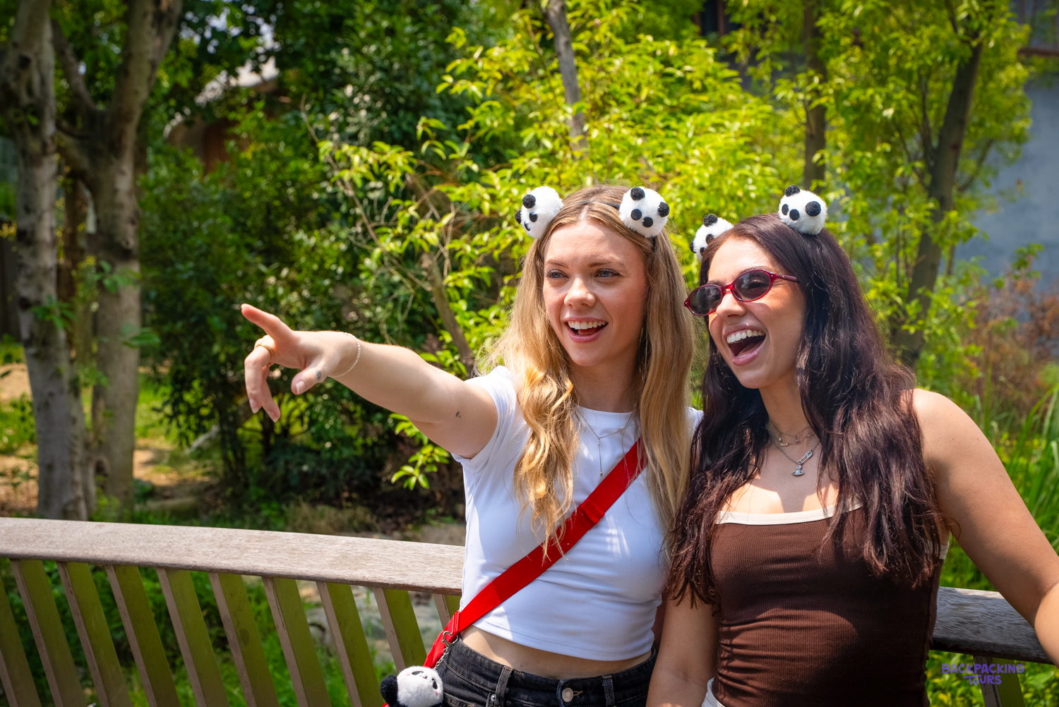 Two travellers wearing panda ear headbands point excitedly at something in the trees.