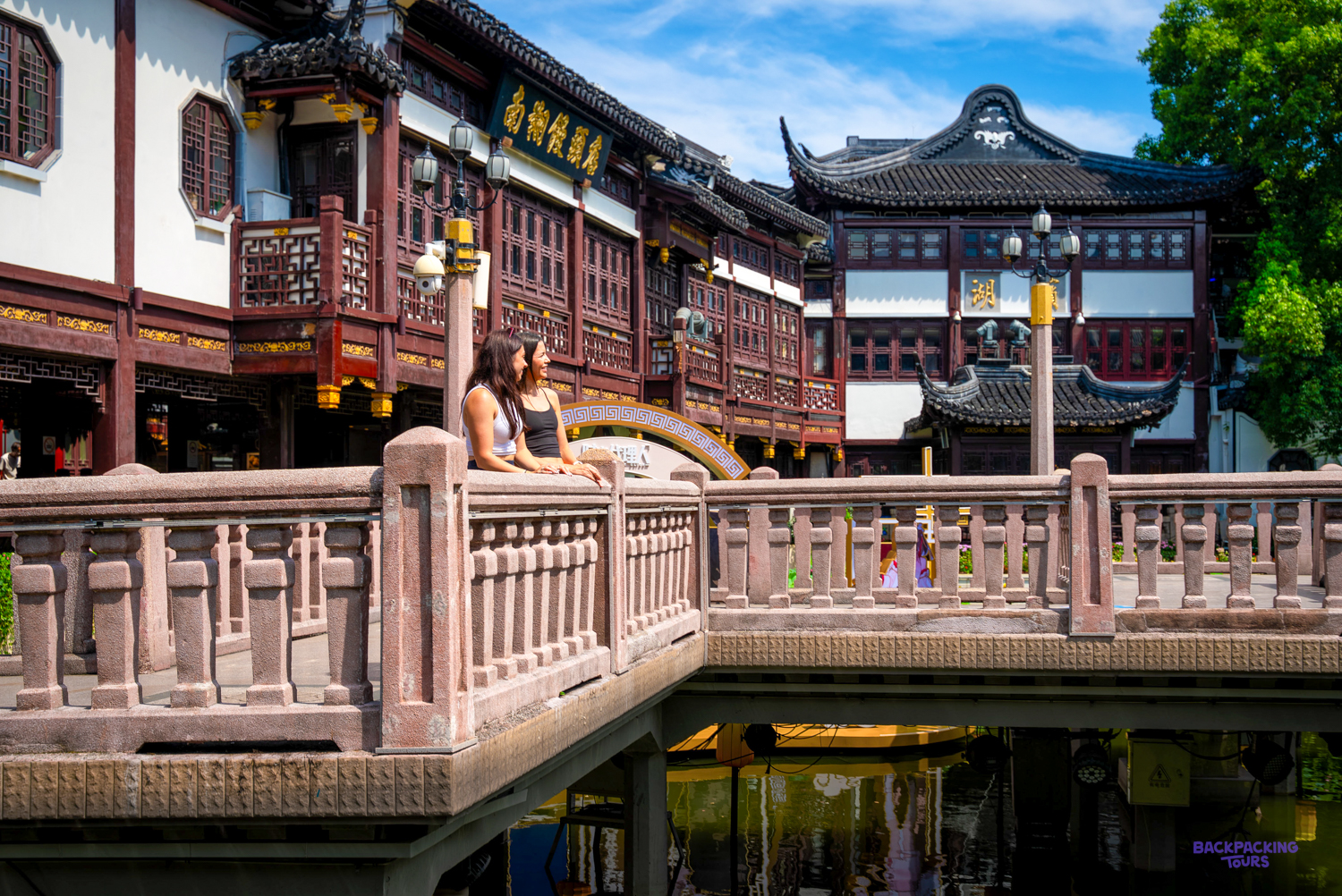 Traditional wooden buildings with upturned eaves above a carved stone balustrade in a classical garden.