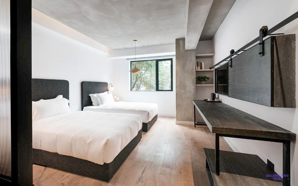 A minimalist twin room with dark headboards, concrete walls and a window onto trees.