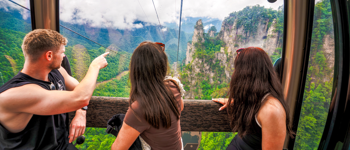 Travellers in a cable car point out at forested sandstone peaks rising from the valley.