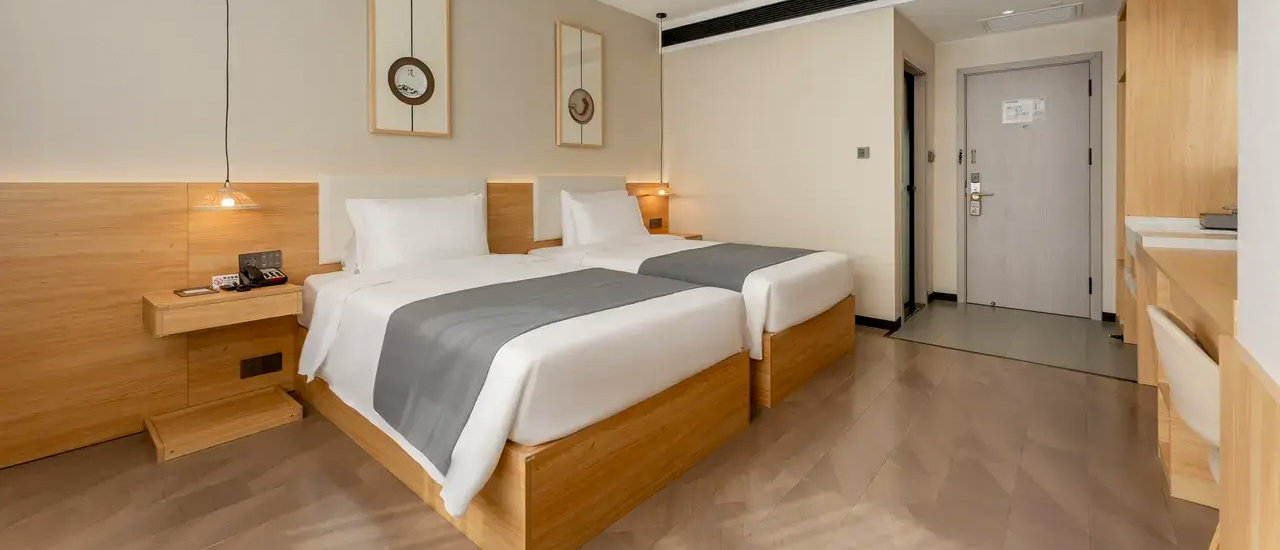 A modern twin room with two single beds, grey runners and light wooden furniture.