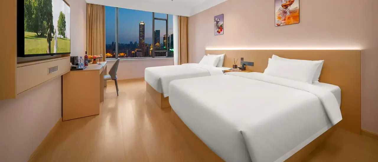 A twin room with two white beds and a floor-to-ceiling window looking out over city towers.