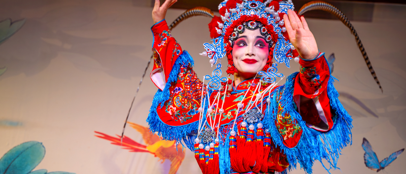 A Sichuan Opera performer in a painted mask and red embroidered costume strikes a pose on stage.
