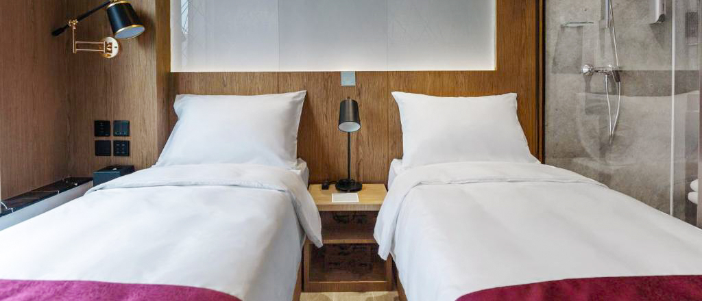 Two single beds with white linen against a wood-panelled wall, beside a glass shower.