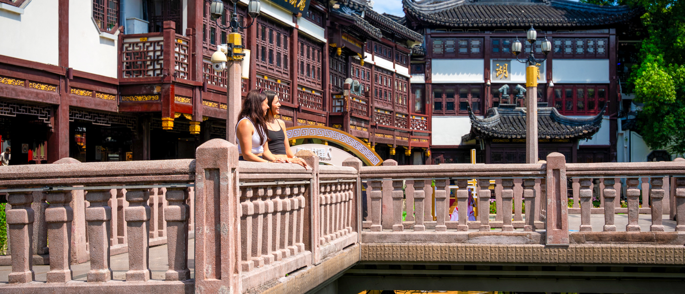 Traditional wooden buildings with upturned eaves above a carved stone balustrade in a classical garden.
