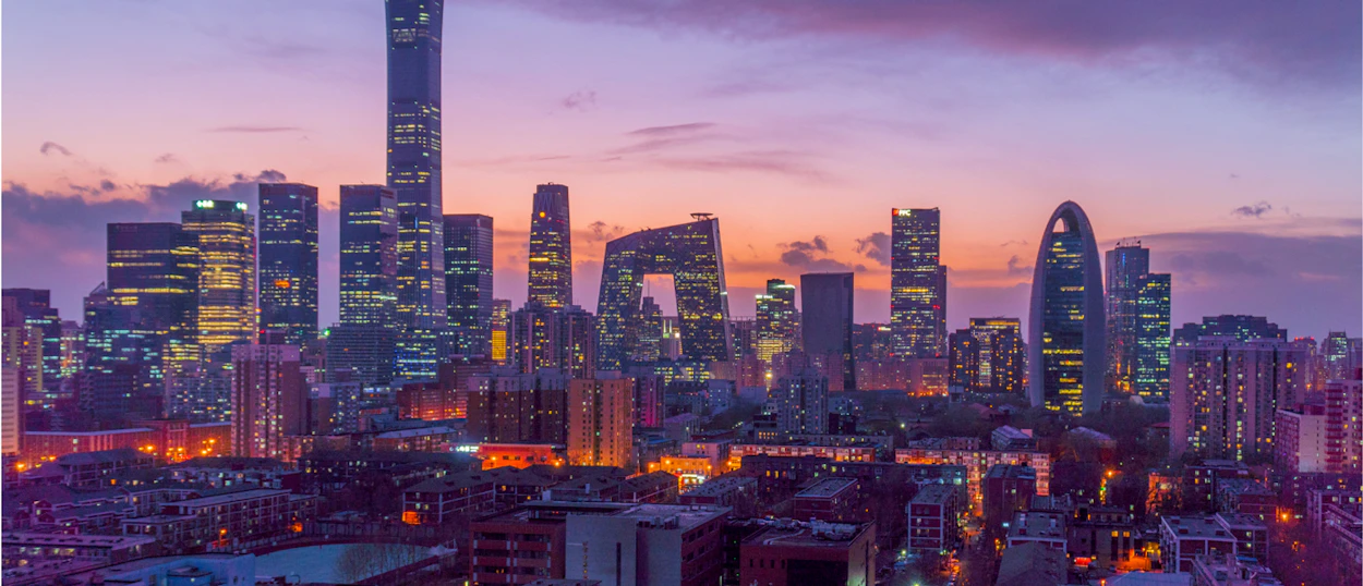 Beijing city skyline at dusk with illuminated skyscrapers and a vibrant purple and orange sky.