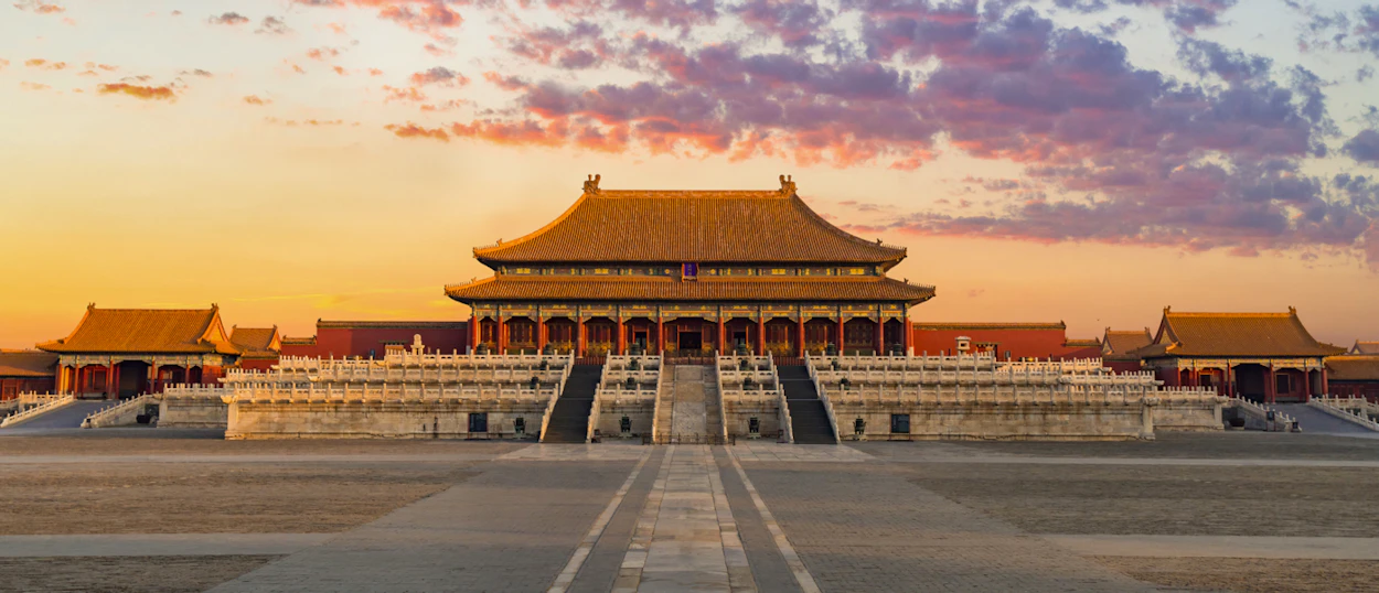 The majestic Forbidden City palace in Beijing glows under a dramatic sunset sky.