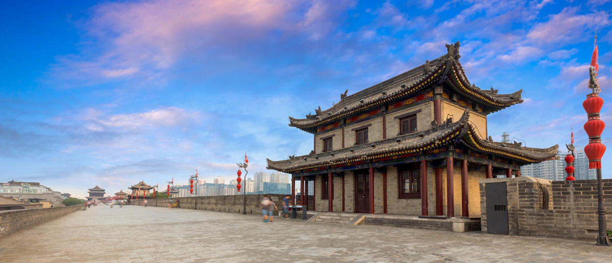 People stroll along the ancient Xi'an City Wall, admiring traditional Chinese architecture under a vibrant sky.