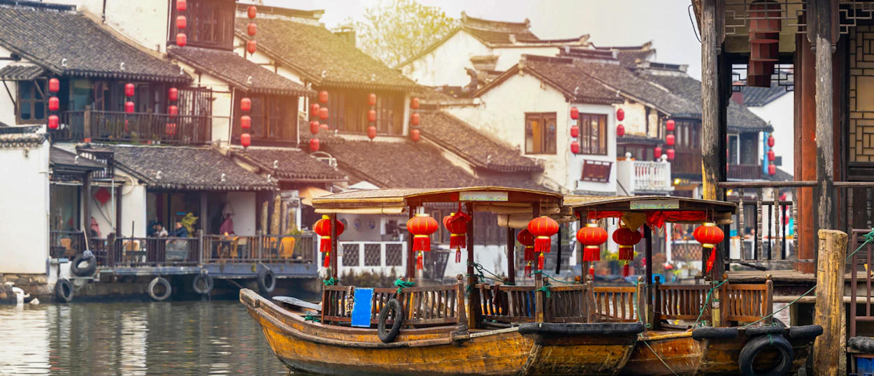 Sunlight illuminates traditional boats and ancient buildings adorned with red lanterns along a Shanghai canal.