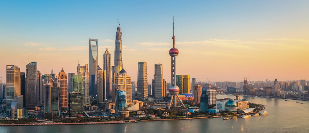 The iconic Shanghai skyline at sunset, with numerous skyscrapers reflecting the golden light over the river.
