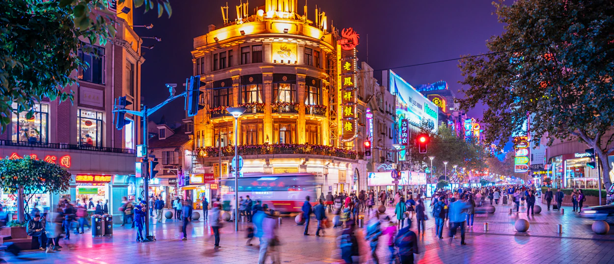 A vibrant Shanghai street at night, with crowds of people and brightly lit buildings.