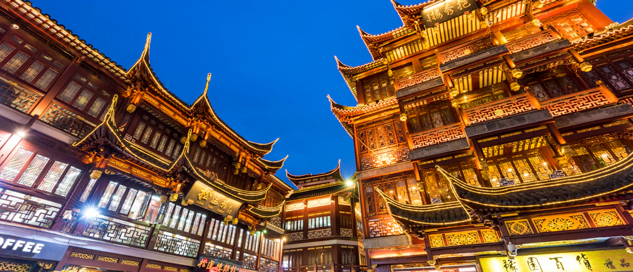 Ornate traditional Chinese buildings with glowing lights under a deep blue evening sky in Shanghai.