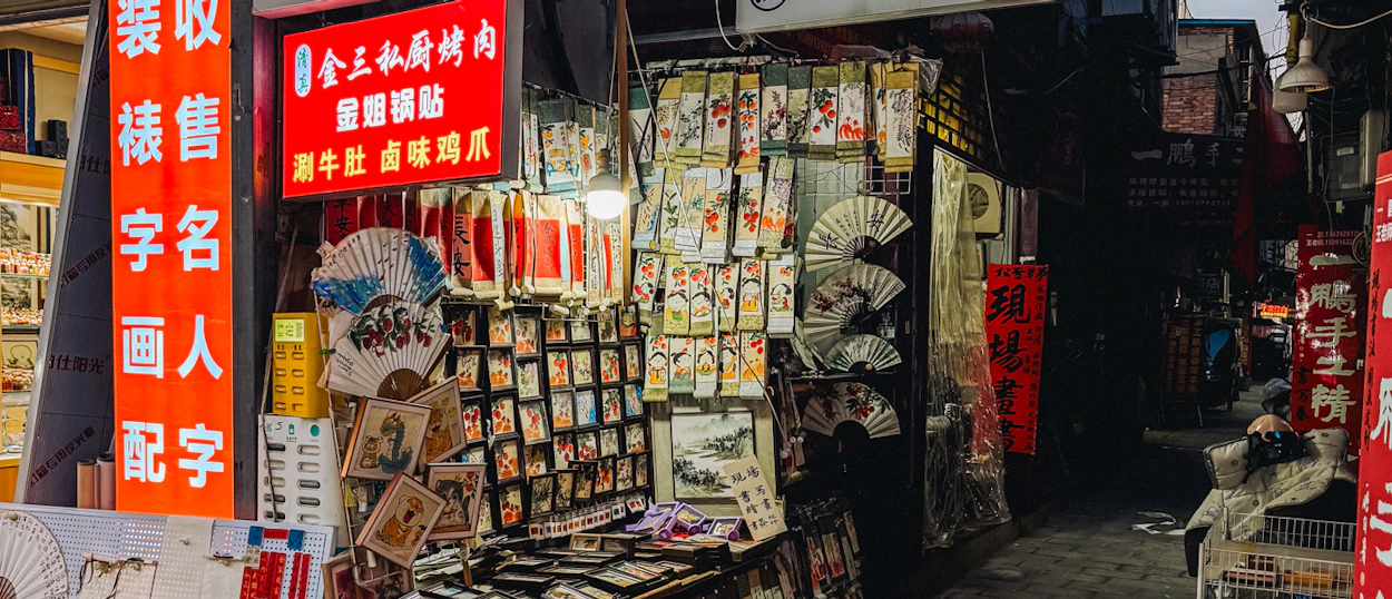 Narrow alleyway in Xi'an with market stalls displaying colorful fans and various souvenirs.