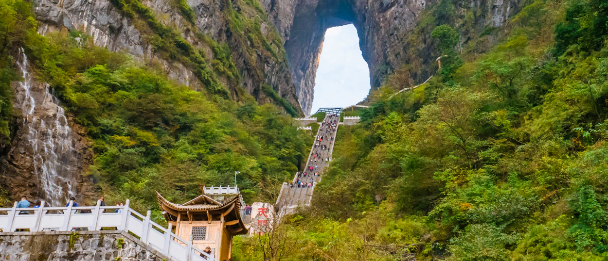 Tourists ascend a long staircase towards the majestic Tianmen Cave in Zhangjiajie, China.