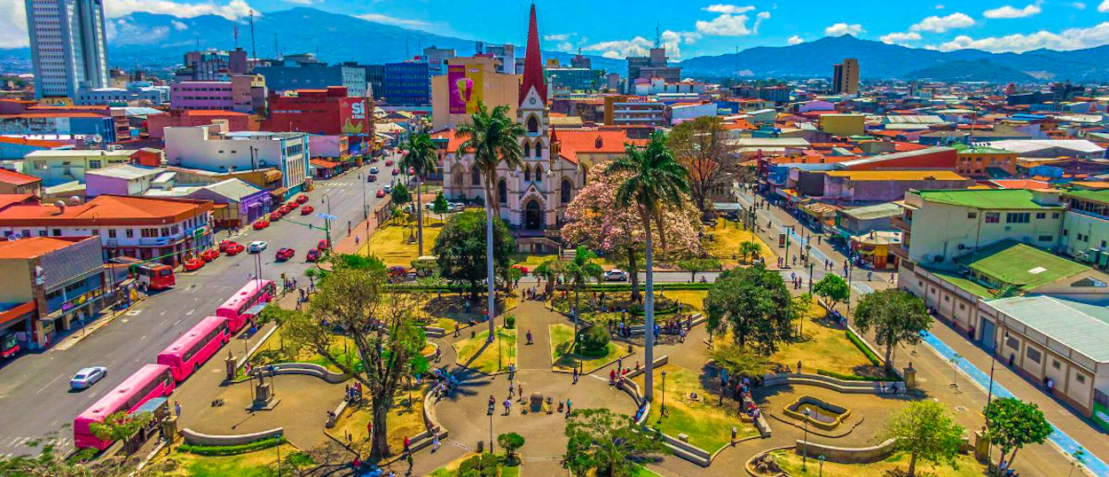 Aerial view of San José, Costa Rica, showing a vibrant city park, church, and colorful buildings.