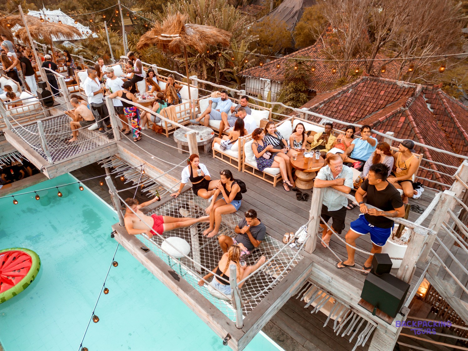 Many people socialising and relaxing at a multi-level outdoor venue with a swimming pool.