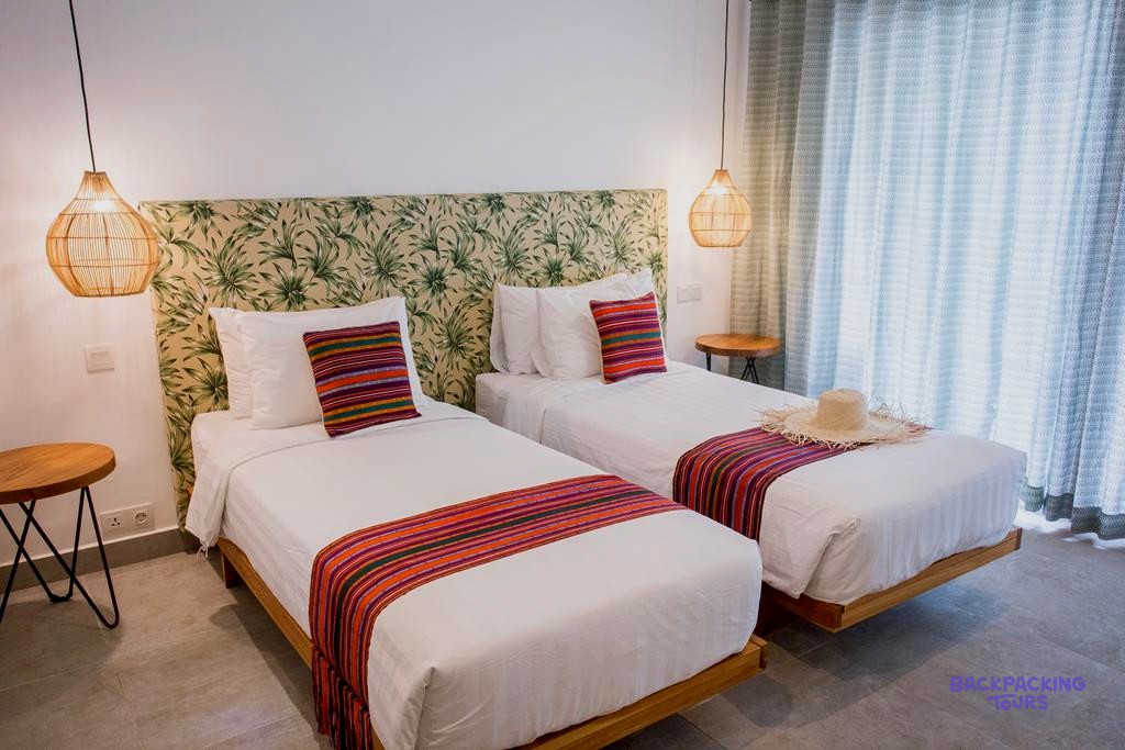 Two single beds with white linen, colourful runners, and leaf-patterned headboards in a bright room.