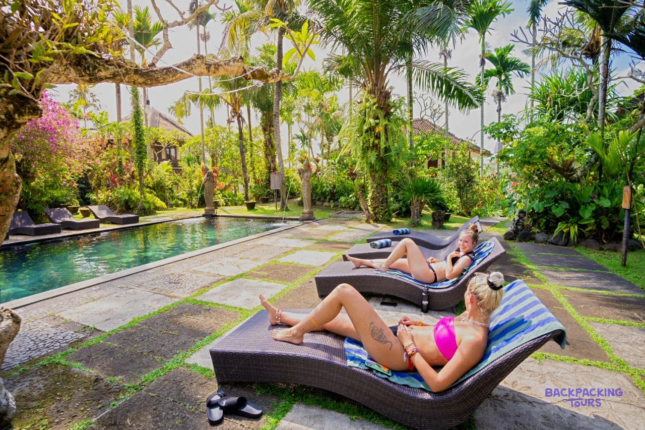 Guests relax on sun loungers next to a beautiful swimming pool in a tropical garden setting.