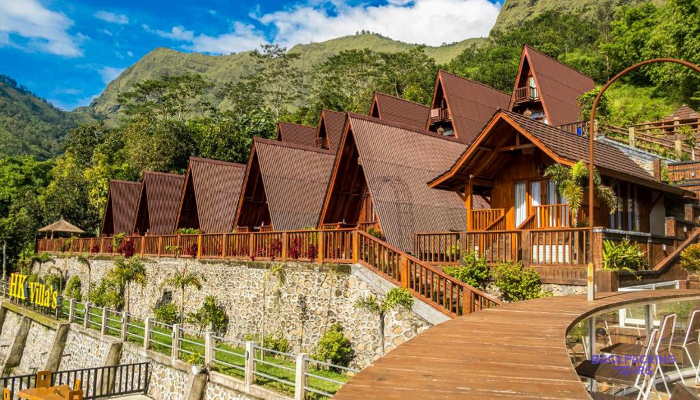 Several wooden A-frame villas with brown roofs are built into a lush green mountain hillside.