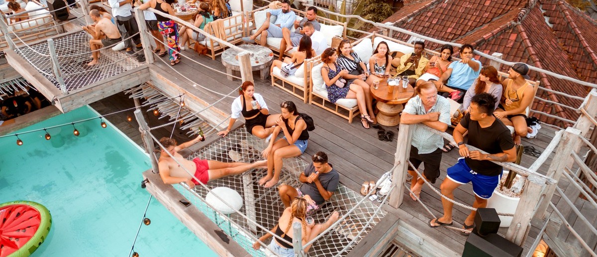 Many people socialising and relaxing at a multi-level outdoor venue with a swimming pool.