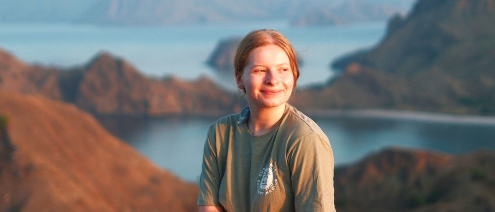 Young woman sits on a rocky viewpoint, overlooking a bay with many hilly islands.