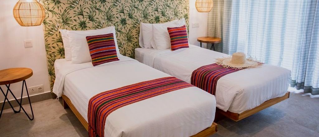 Two single beds with white linen, colourful runners, and leaf-patterned headboards in a bright room.