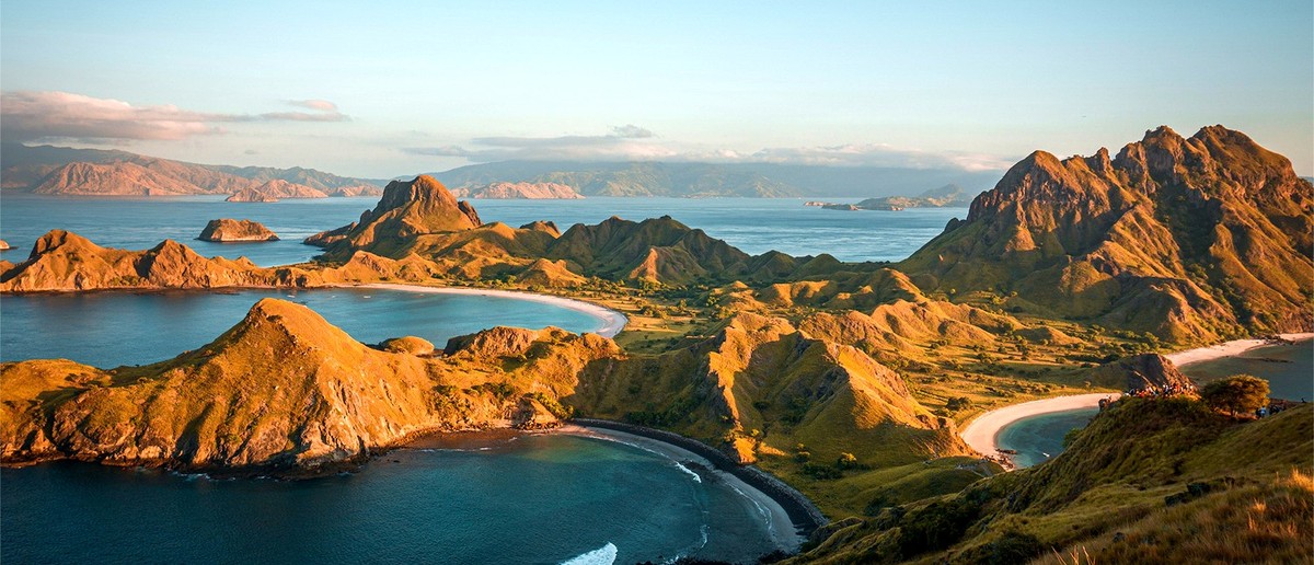 Golden hills and white sand beaches curve around turquoise bays, with many islands visible under a clear sky.