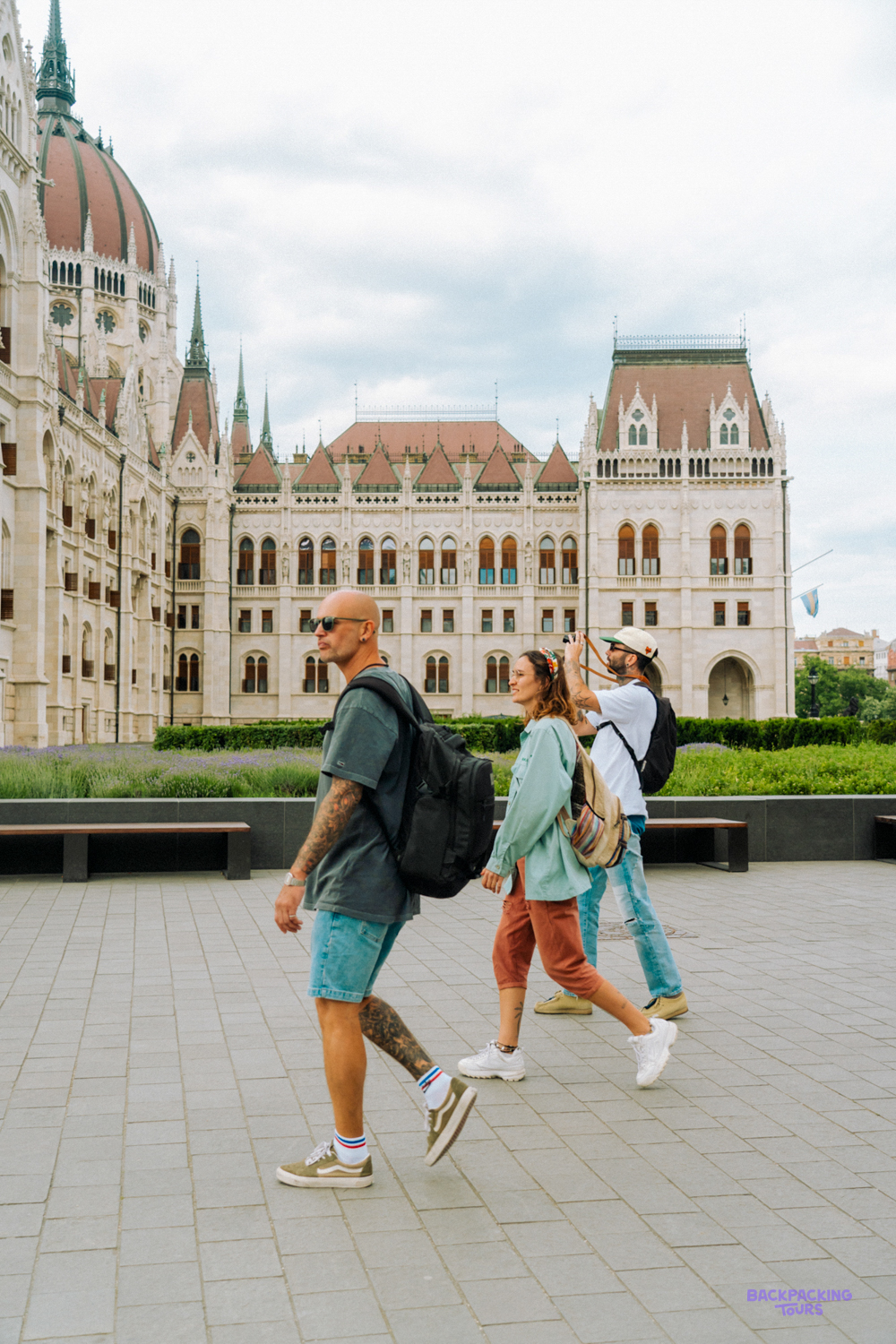 Three travellers with backpacks walk past the Hungarian Parliament building in Budapest.
