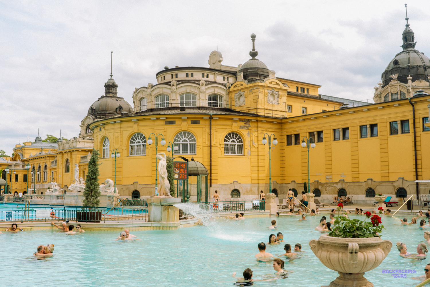 Bathers in the outdoor pool in front of the yellow Széchenyi Thermal Baths building in Budapest.