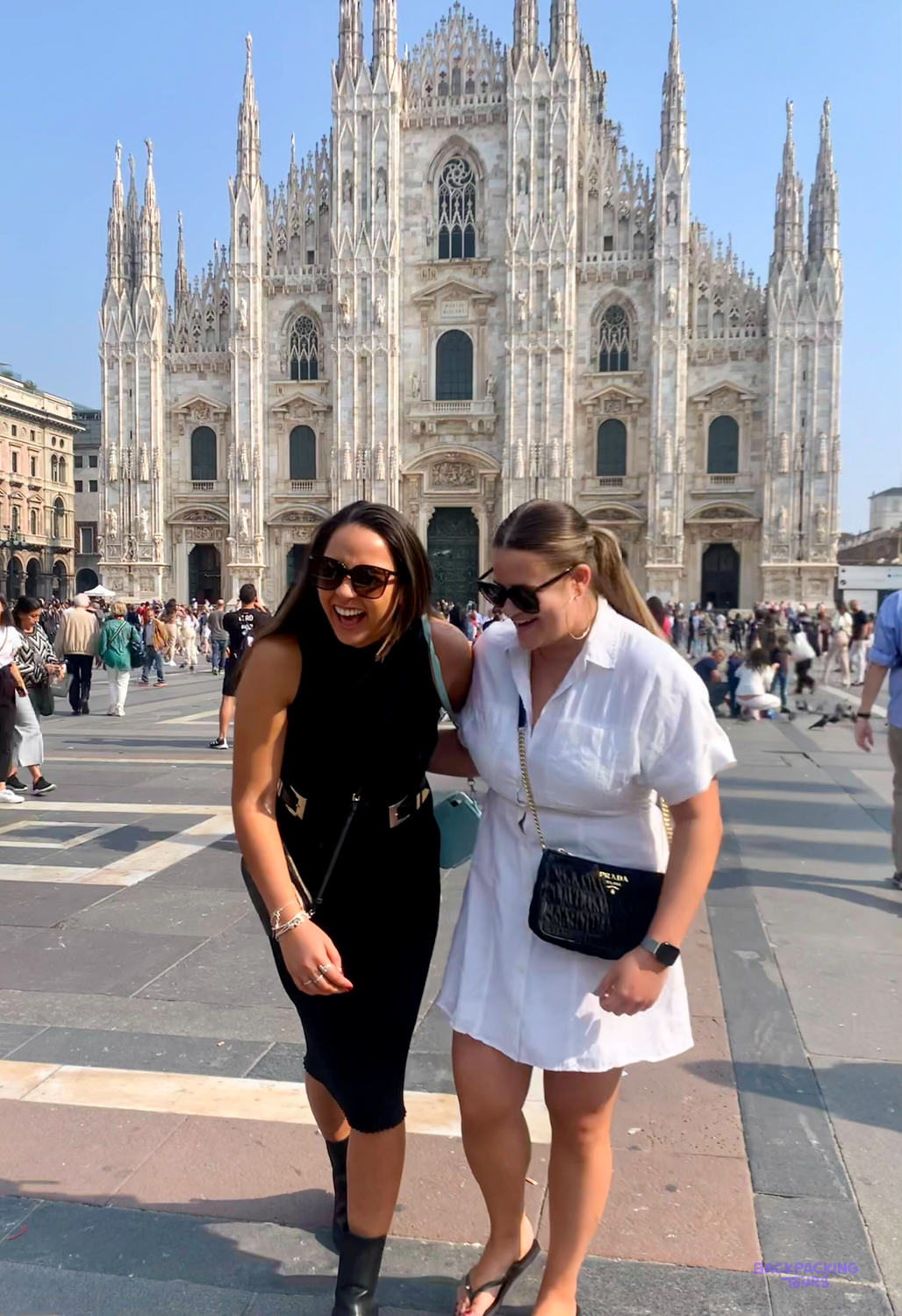 Two friends laugh together in Piazza del Duomo with Milan Cathedral behind them.