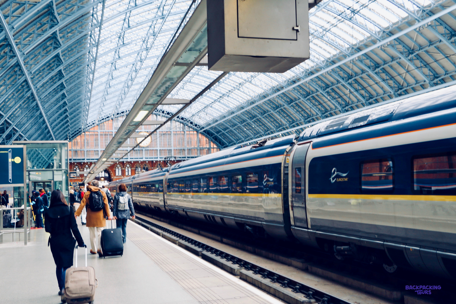 Travellers with backpacks and suitcases walk along a station platform beside a high-speed train.