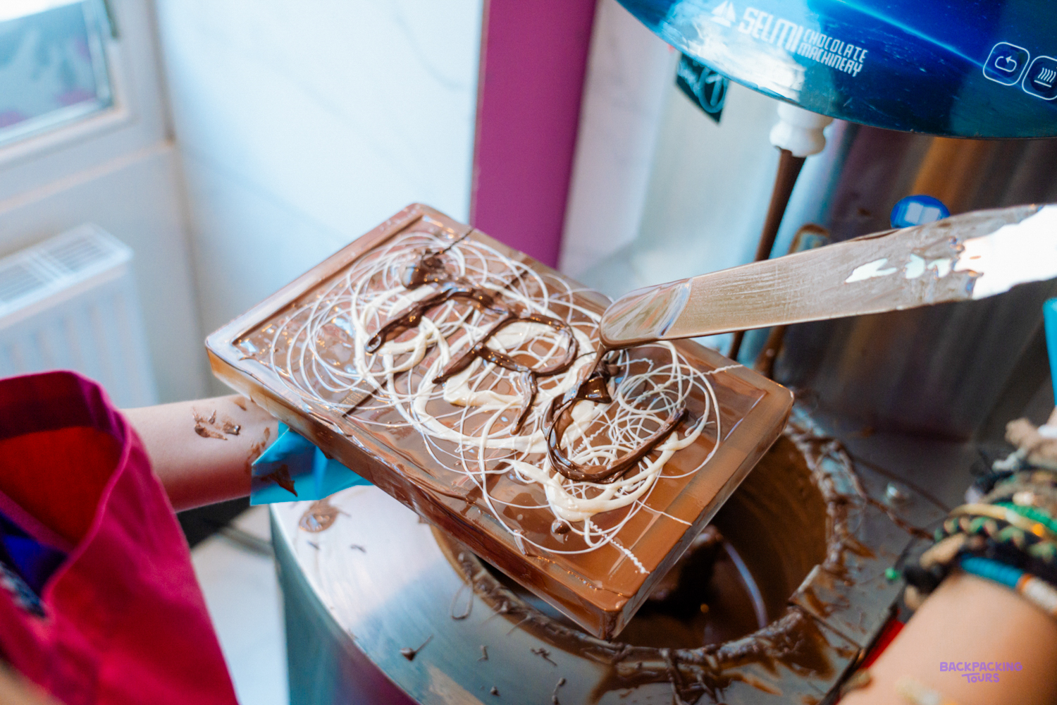 A hand decorates a bar of chocolate with swirls of white and dark chocolate.