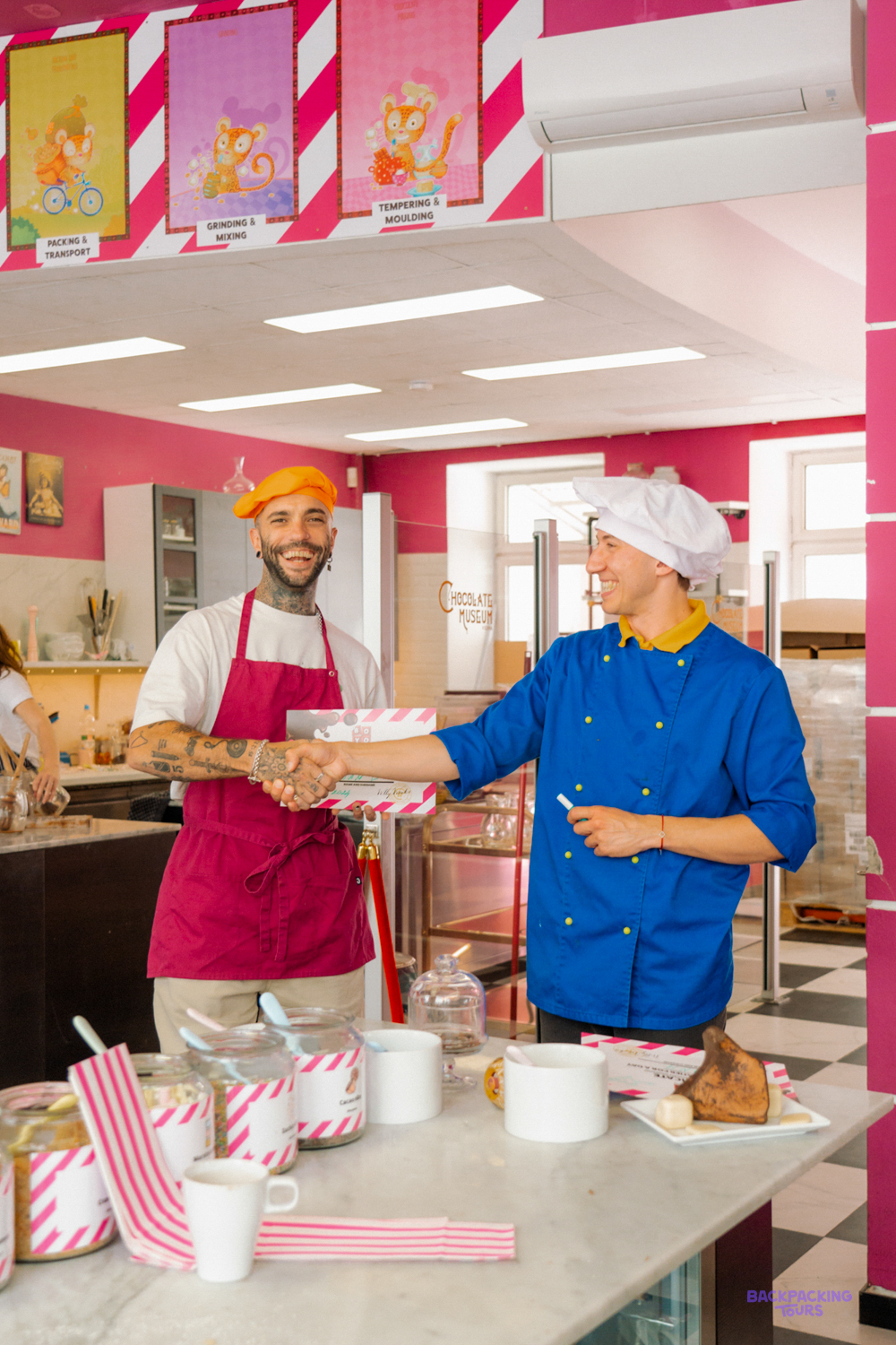A traveller in an apron shakes hands with a chocolatier during a chocolate-making workshop.