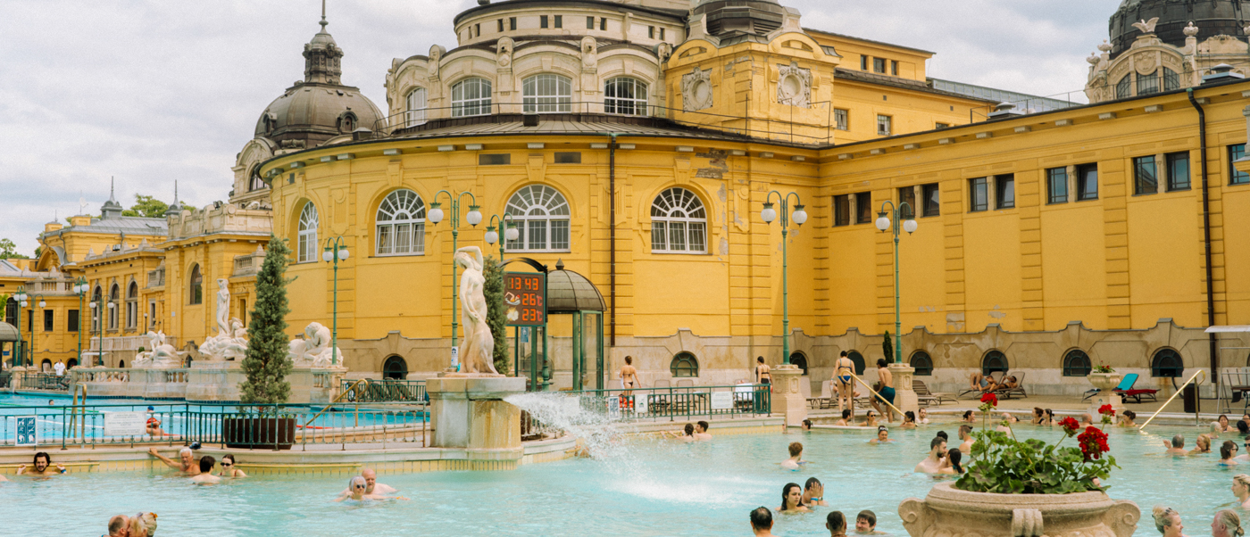 Bathers in the outdoor pool in front of the yellow Széchenyi Thermal Baths building in Budapest.