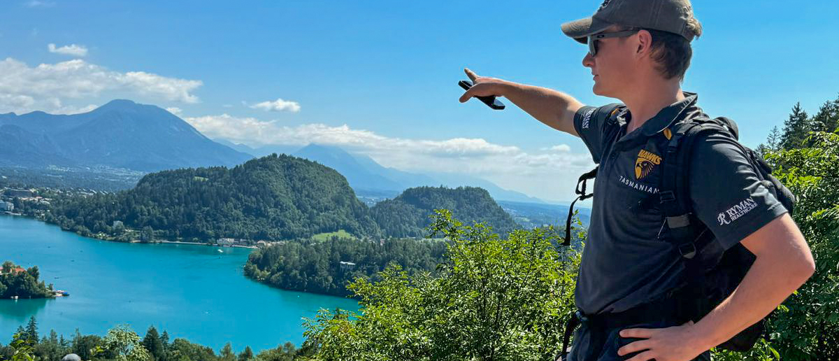 A man on a rocky viewpoint points out over the turquoise water of Lake Bled.