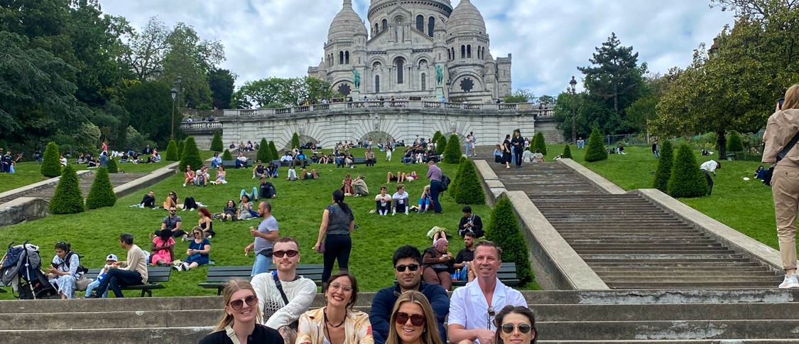 Travellers sit together on the steps below the white domes of the Sacré-Cœur in Montmartre.