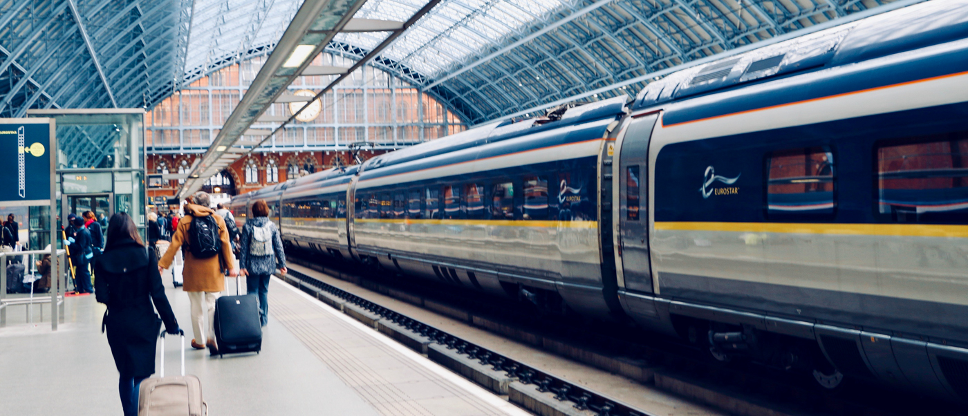 Travellers with backpacks and suitcases walk along a station platform beside a high-speed train.