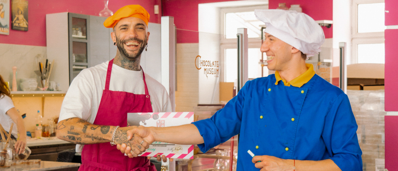 A traveller in an apron shakes hands with a chocolatier during a chocolate-making workshop.