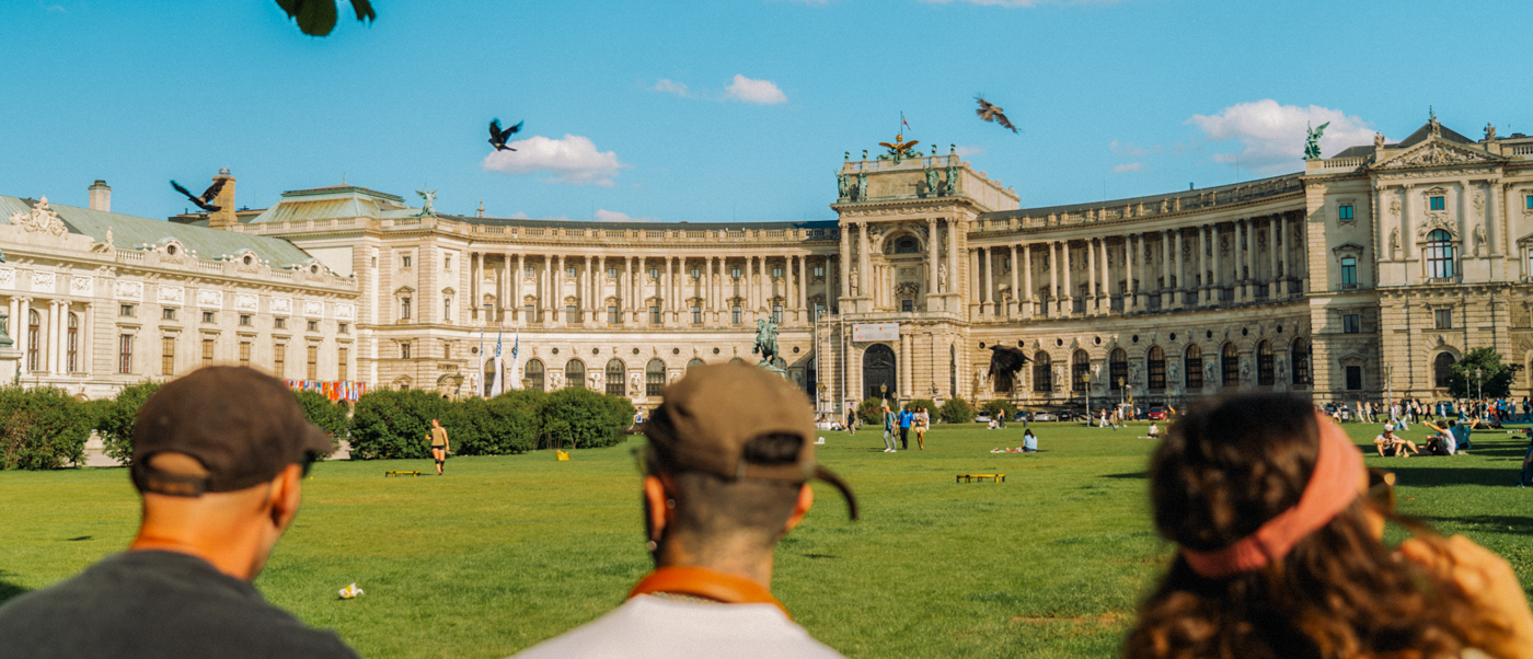 Travellers look across a sunny lawn towards the curved front of the Hofburg Palace in Vienna.