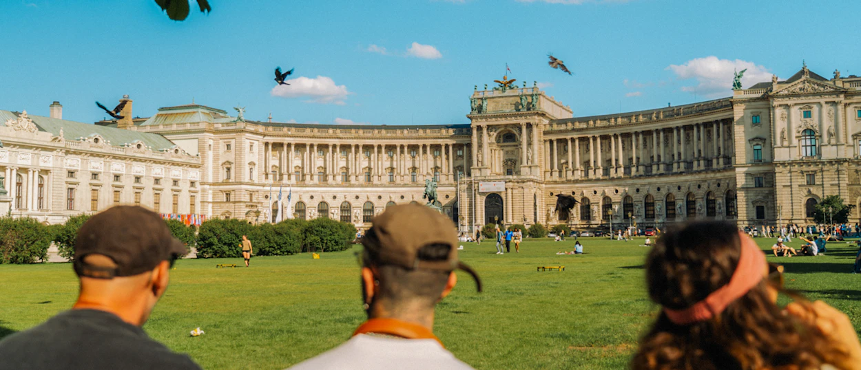 Travellers look across a sunny lawn towards the curved front of the Hofburg Palace in Vienna.