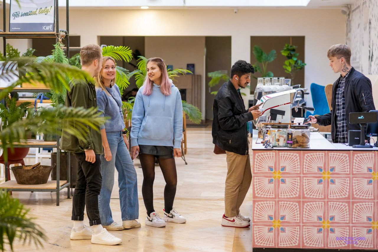 Travellers chatting by the coffee counter and plants in the lobby of the Budapest hostel