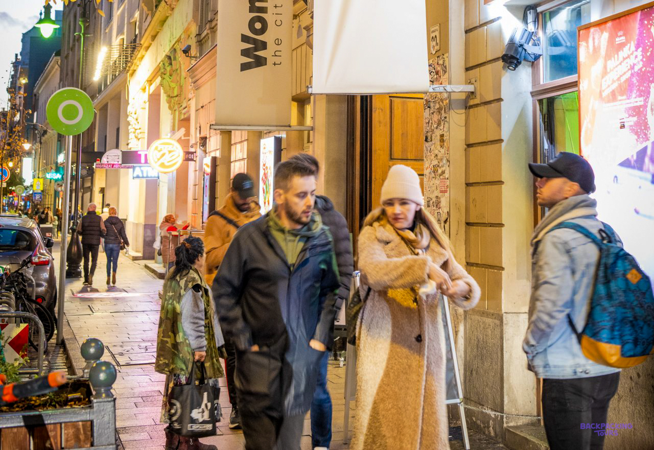 Travellers wrapped up in coats outside the entrance of the Budapest hostel on a lit-up street