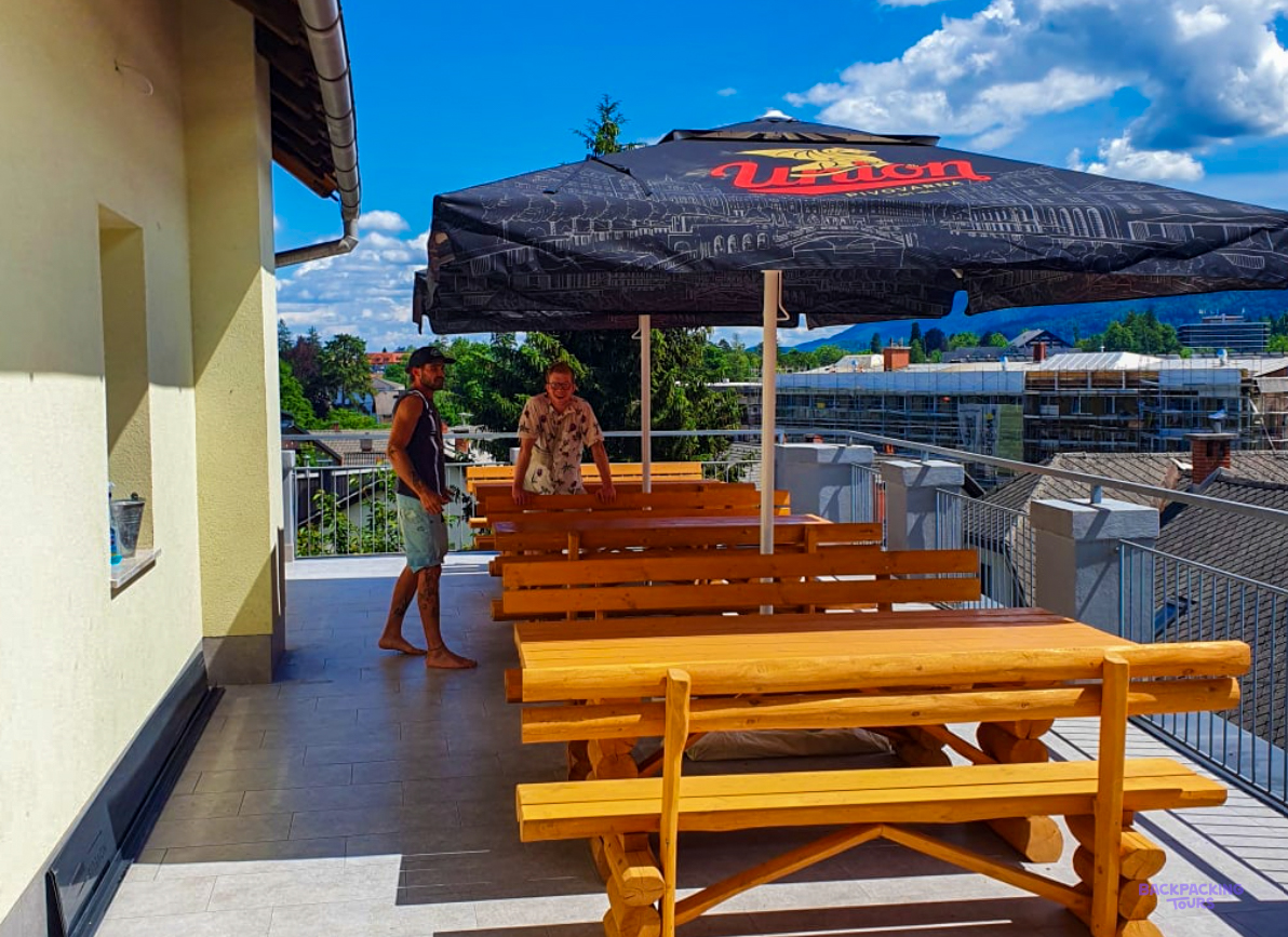 A rooftop terrace with wooden picnic tables and a parasol at the hostel in Lake Bled