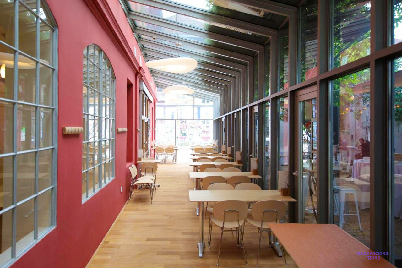 A long glass-walled dining room with red walls and wooden tables at the Ljubljana hostel