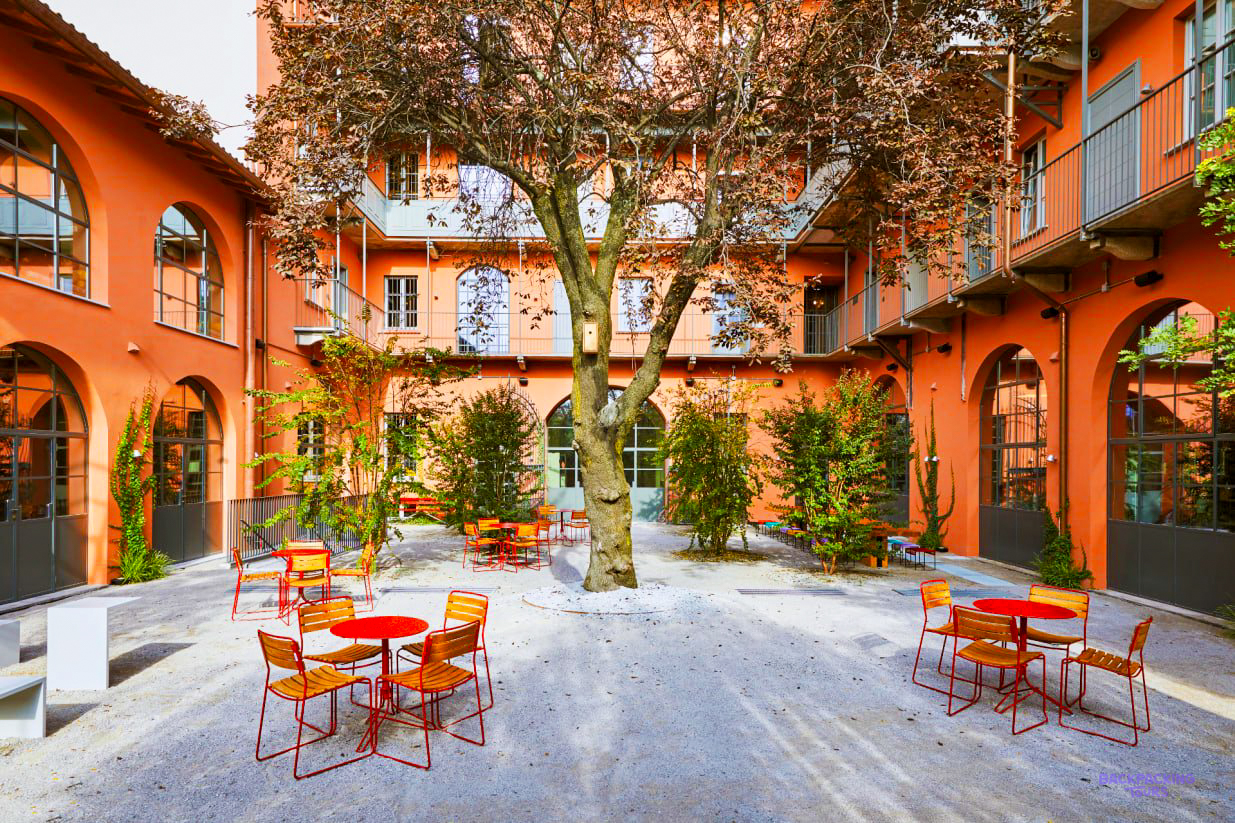 The orange courtyard of the Milan hostel, with red tables and chairs around a tree