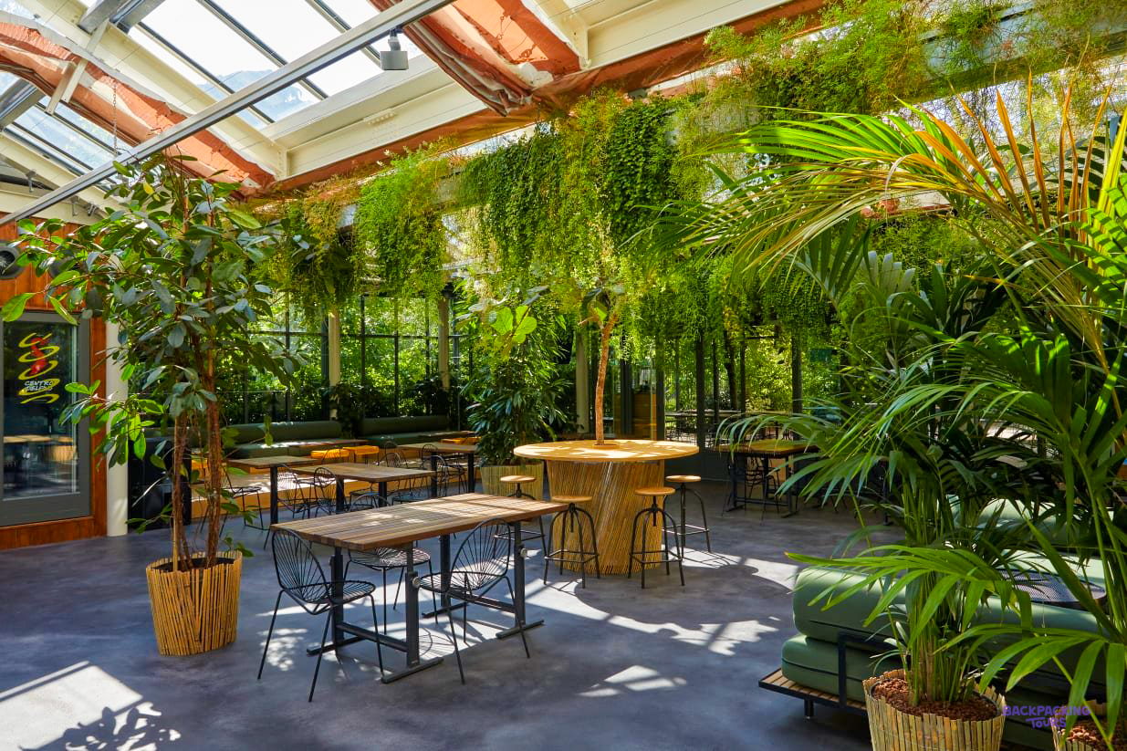 A glass-roofed dining area full of tropical plants at the Milan hostel
