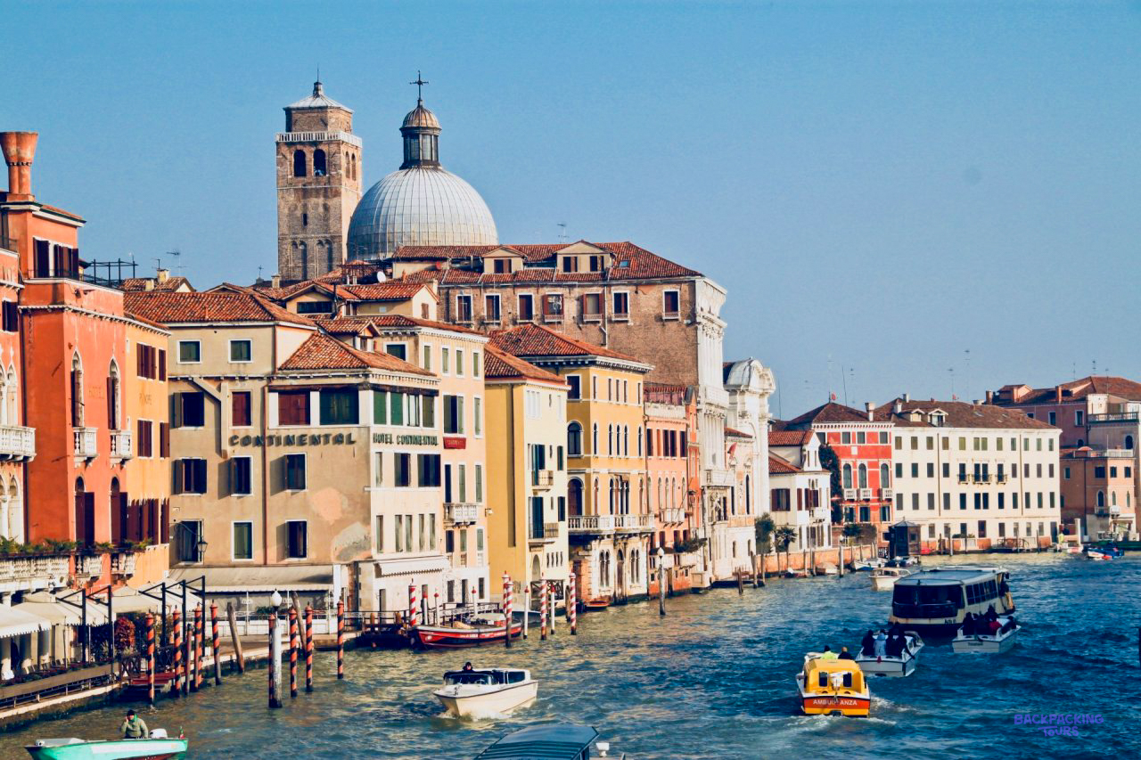 Colourful palaces and boats along the Grand Canal in Venice, with a church dome behind