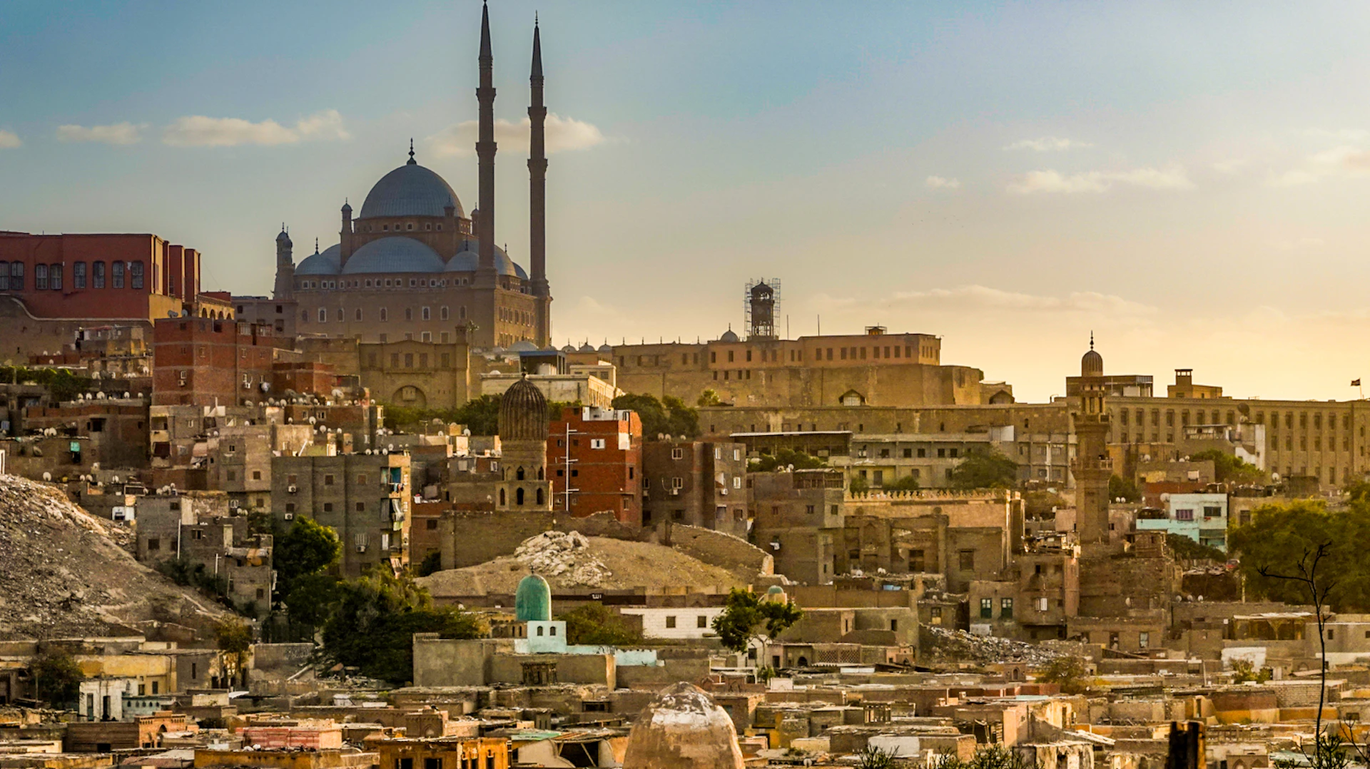 Warm sunset light illuminates the historic cityscape of Cairo, featuring the iconic Muhammad Ali Mosque.