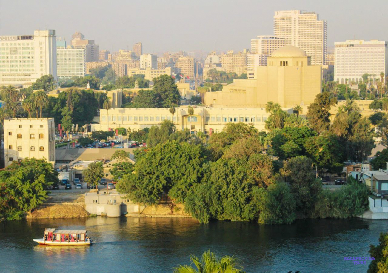 A small boat on the Nile below the trees and tower blocks of Cairo