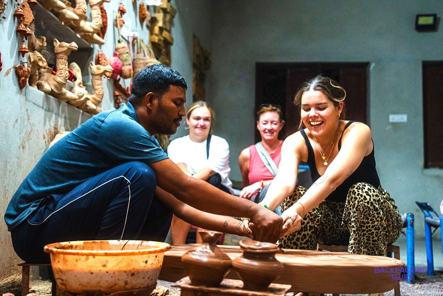 A man and a woman are making pottery on a wheel, with three other people watching.